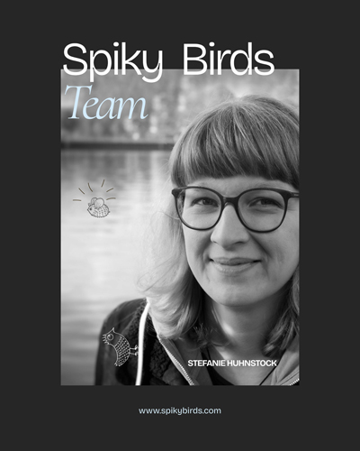 Die Schwarzweißfotografie zeigt eine Person, die lächelt. Die Person ist weiß, trägt eine Brille, hat schulterlanges Haar und trägt eine schwarze Jacke über einem hellen Hoodie. Auf dem Foto sind kleine Zeichnungen einer Biene und eines kleinen Vogels platziert. Im Hintergrund sind Wasser und ein Ufer.Weiße Schrift auf dunklem Grund titelt: "Spiky Birds. Team. Stefanie Huhnstock."